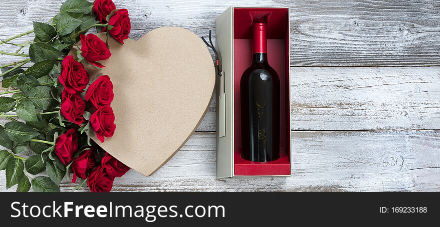 Happy Valentines Day celebration with wine, red roses and a heart shaped gift box on white rustic wood. Happy Valentines Day celebration with wine, red roses and a heart shaped gift box on white rustic wood