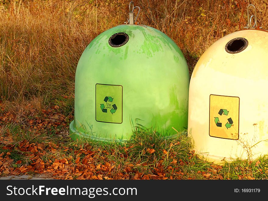 Two colorful recycling bins in a autumn park.