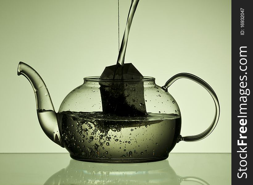 Water pouring into a teapot with a teabad in the pot. Green background. Water pouring into a teapot with a teabad in the pot. Green background.
