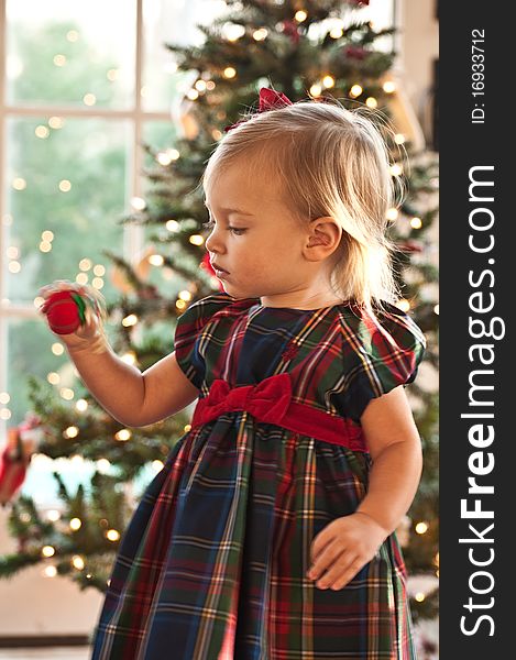 Little Girl Twisting an Ornament in front of a Christmas Tree. Little Girl Twisting an Ornament in front of a Christmas Tree
