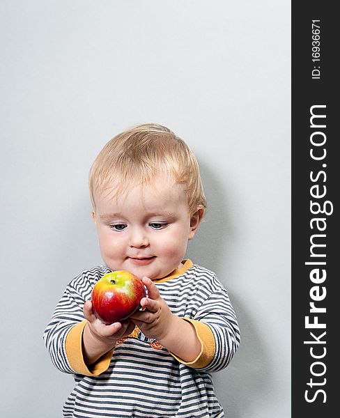 Charming baby with apple on a grey background