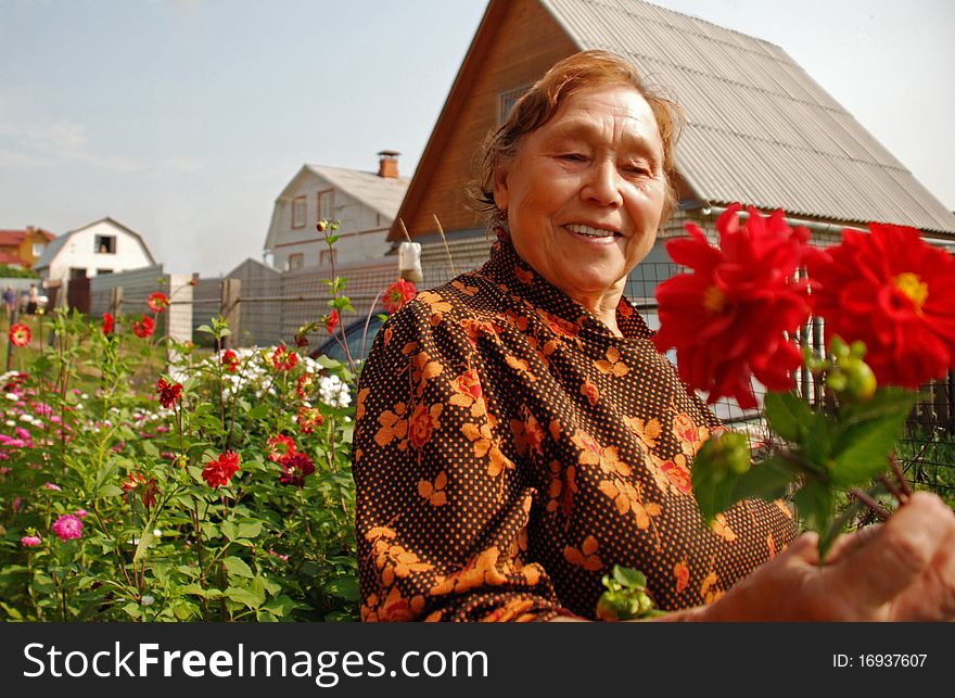 The elderly woman with pride looks at the grown up flowers near to its summer residence. The elderly woman with pride looks at the grown up flowers near to its summer residence