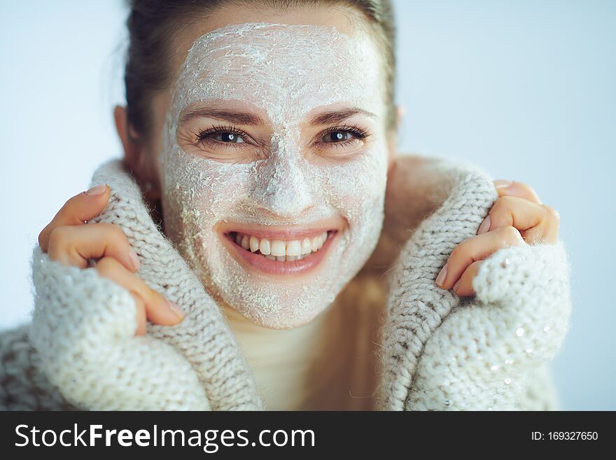 Smiling stylish woman in roll neck sweater and cardigan with white facial mask covering in clothes on winter light blue background. Smiling stylish woman in roll neck sweater and cardigan with white facial mask covering in clothes on winter light blue background