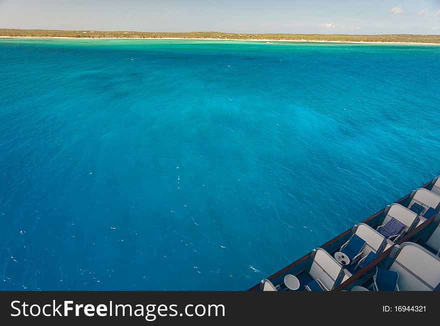 Caribbean island view from cruise ship deck. Contains intense blue water, island and part of cruise ship decks.