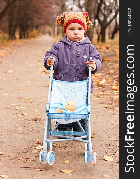 Beautiful baby with a stroller in a funny hat outdoor against autumn nature