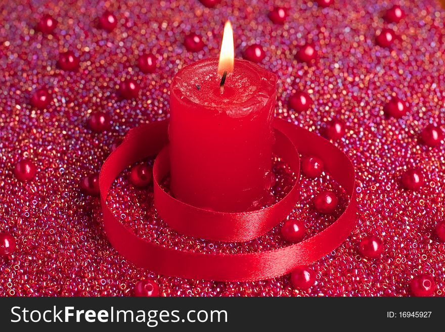 Burning candle circled with red ribbon placed on beads. Burning candle circled with red ribbon placed on beads