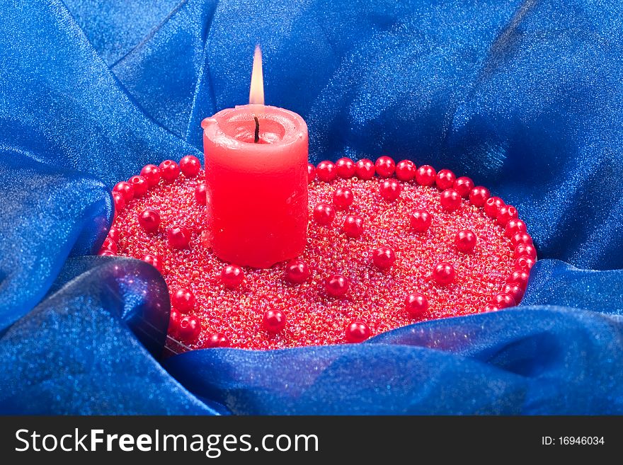 Burning candle with red ribbon placed on beads. Burning candle with red ribbon placed on beads