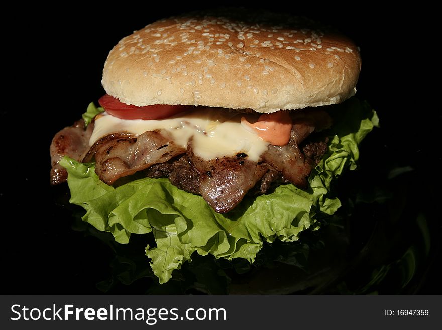 Tasty burger on a black, slightly reflective glass plate. Tasty burger on a black, slightly reflective glass plate