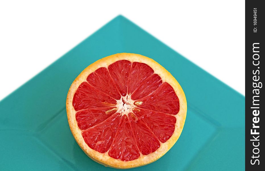 Half a red grapefruit in a square plate shot on white background with angle showing simple geometrical shapes. Half a red grapefruit in a square plate shot on white background with angle showing simple geometrical shapes.