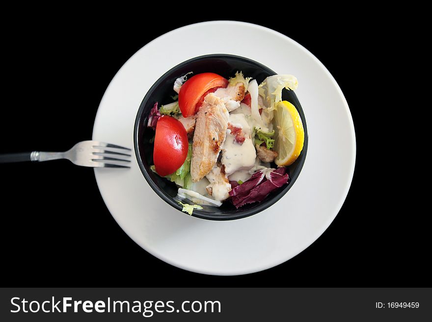 Portion of a mixed salad with chicken, tomatoes, various lettuce, bacon bits, lemon, Caesar sauce - shot on black background. Portion of a mixed salad with chicken, tomatoes, various lettuce, bacon bits, lemon, Caesar sauce - shot on black background.