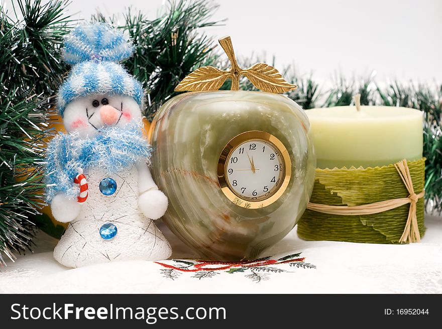 Snowman, candle and Desktop clock shows three minutes before the New year with Christmas garlands. Snowman, candle and Desktop clock shows three minutes before the New year with Christmas garlands