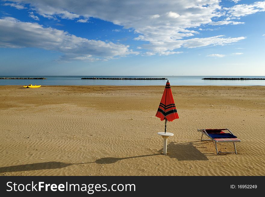 A view over deserted beach in early morning with umbrella and sunbed in foreground and a yellow rowbot in background
