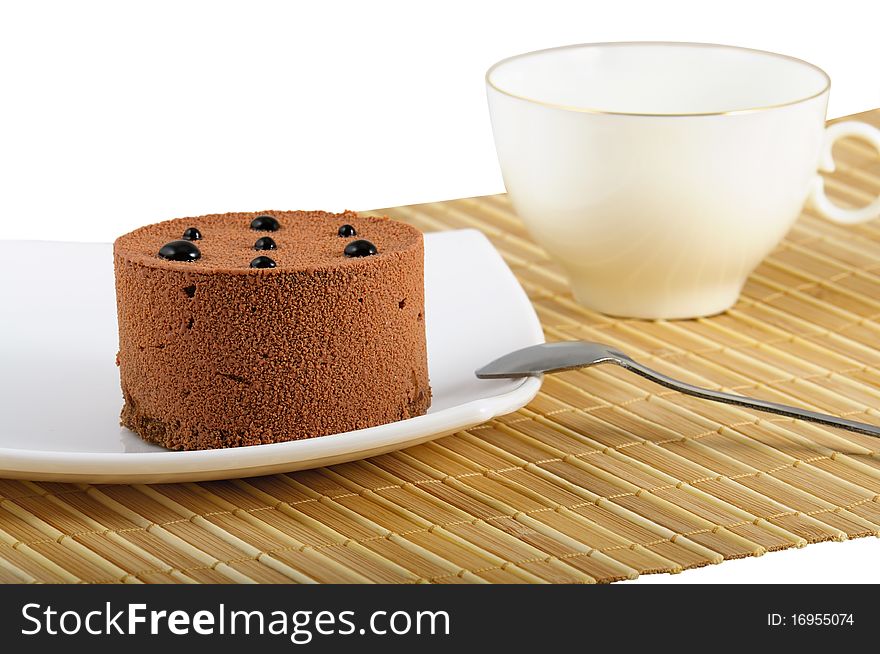 The cake lays on a white plate. Beside a teaspoon and hardly far away a white cup of tea. Closeup. The cake lays on a white plate. Beside a teaspoon and hardly far away a white cup of tea. Closeup