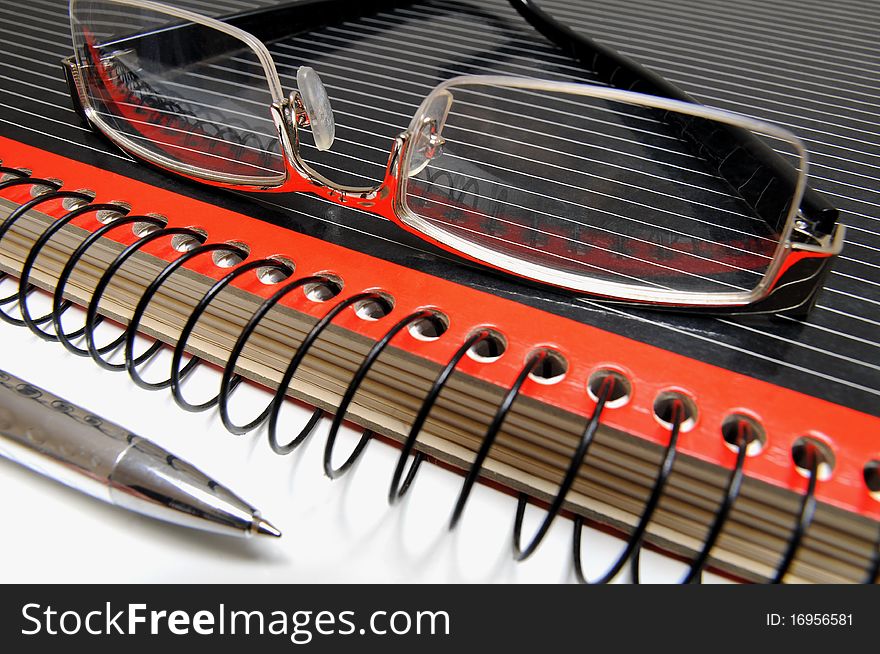Black and red colored ring binder, glasses and ball point. Black and red colored ring binder, glasses and ball point