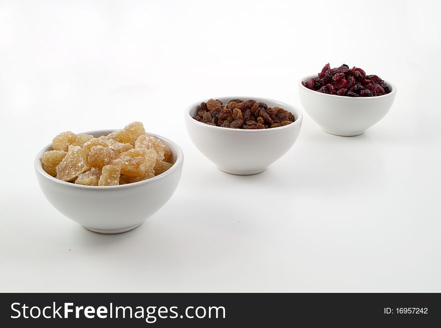 Three bowls containing cake ingredients, ginger, Raisin, cranberries on white backgorund. Three bowls containing cake ingredients, ginger, Raisin, cranberries on white backgorund