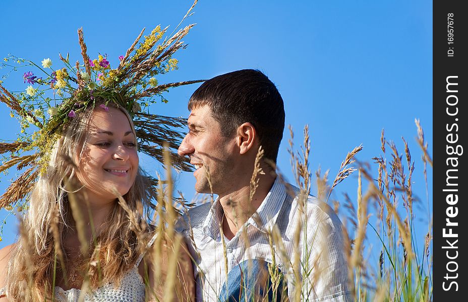 The man and the woman in a wreath, sit on a grass, smile and look against each other enamoured eyes. The man and the woman in a wreath, sit on a grass, smile and look against each other enamoured eyes