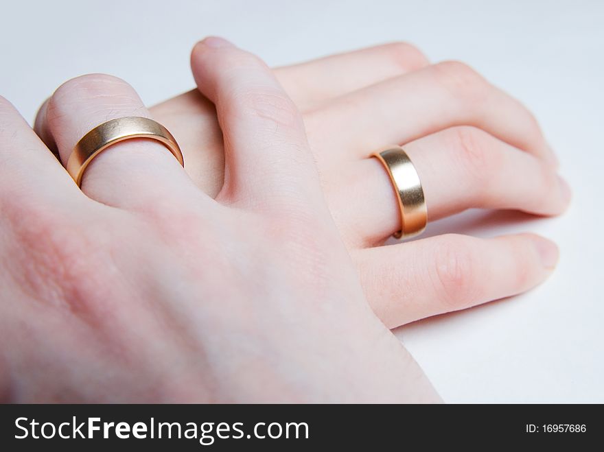 The hand of a man is gently holding the hand of a woman, both wearing golden wedding rings. The hand of a man is gently holding the hand of a woman, both wearing golden wedding rings