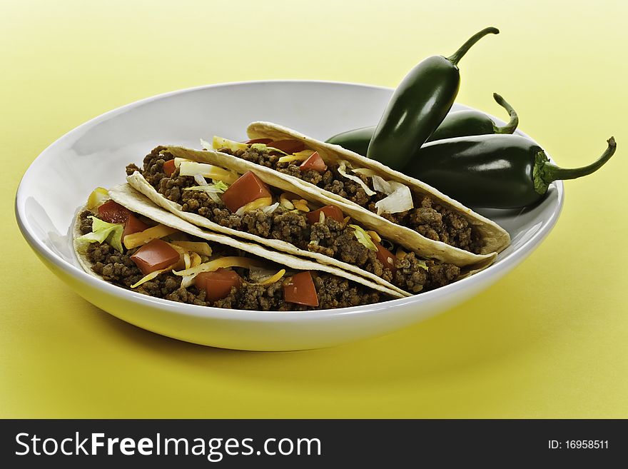 Taco wrap with beef meat in a white plate. Green hot pepper on the side. Yellow background. Taco wrap with beef meat in a white plate. Green hot pepper on the side. Yellow background.