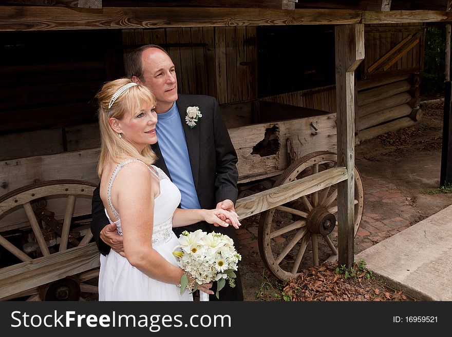 Bride and groom outside standing in front of old wagon.