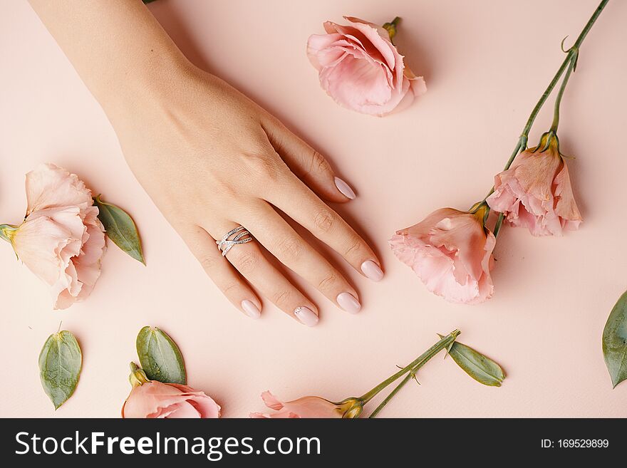 Close up of an elegant diamond ring on young woman finger. Woman hands with manicure and jewelry ring on pink background with flowers, beauty style concept. Close up of an elegant diamond ring on young woman finger. Woman hands with manicure and jewelry ring on pink background with flowers, beauty style concept.