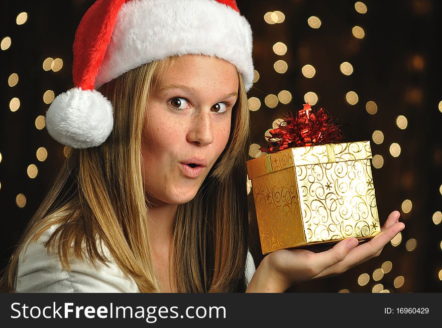 Teen girl wearing a Santa hat holds a golden wrapped gift. Teen girl wearing a Santa hat holds a golden wrapped gift.
