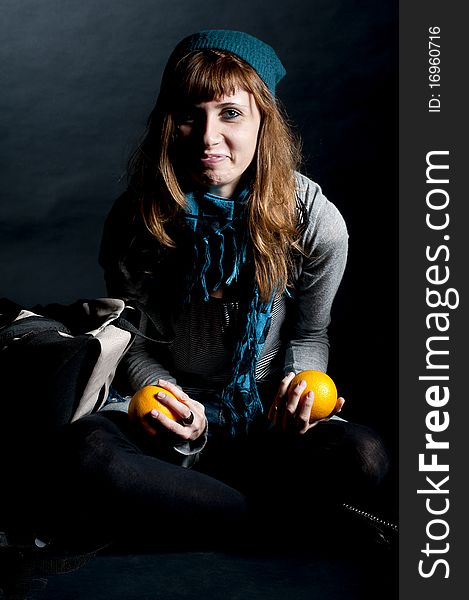 Beautiful girl with scarf and hat and oranges on a black background