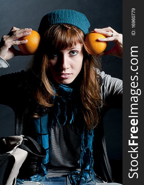Beautiful girl with scarf and hat and oranges on a black background