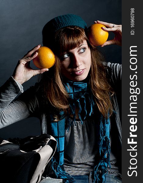 Beautiful girl with scarf and hat and oranges on a black background