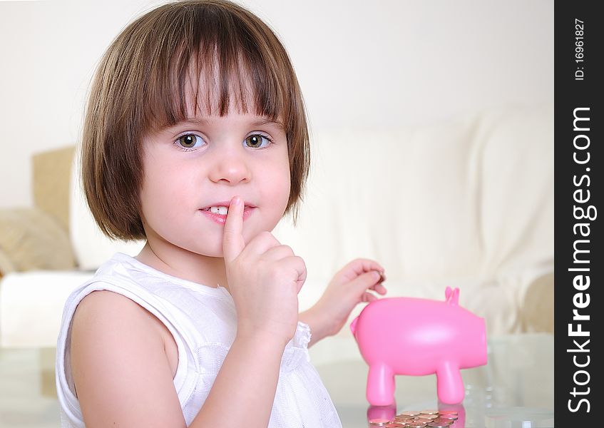 A little girl hides her money in the pig piggy bank.