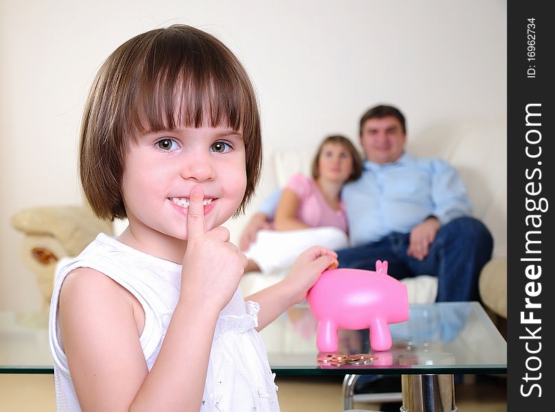 A little girl hides her money in the pig piggy bank.