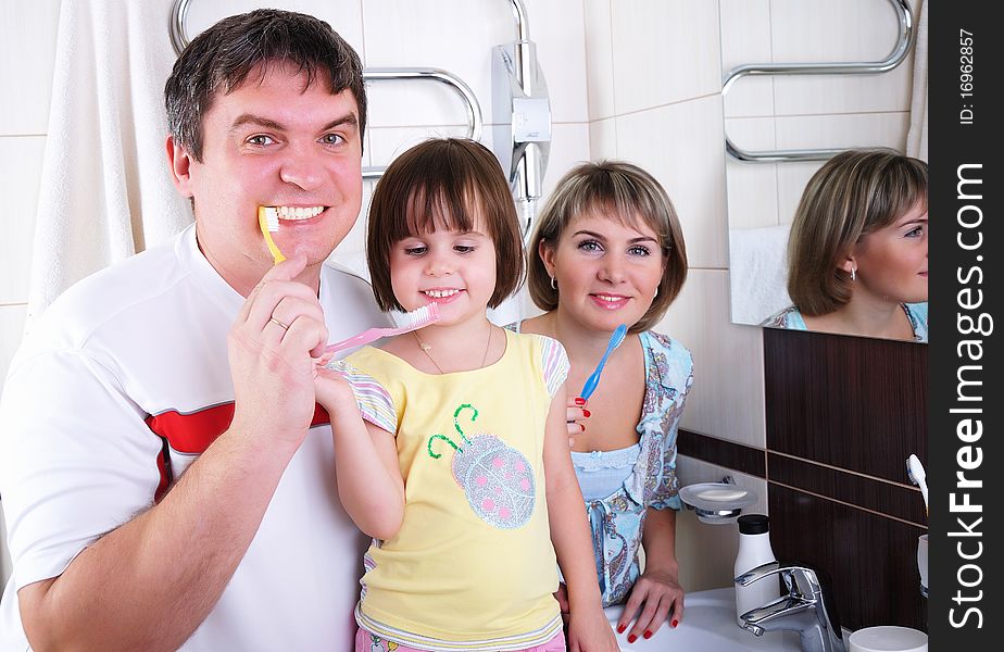 Mom, daughter and father brush their teeth in the bathroom early in the morning.