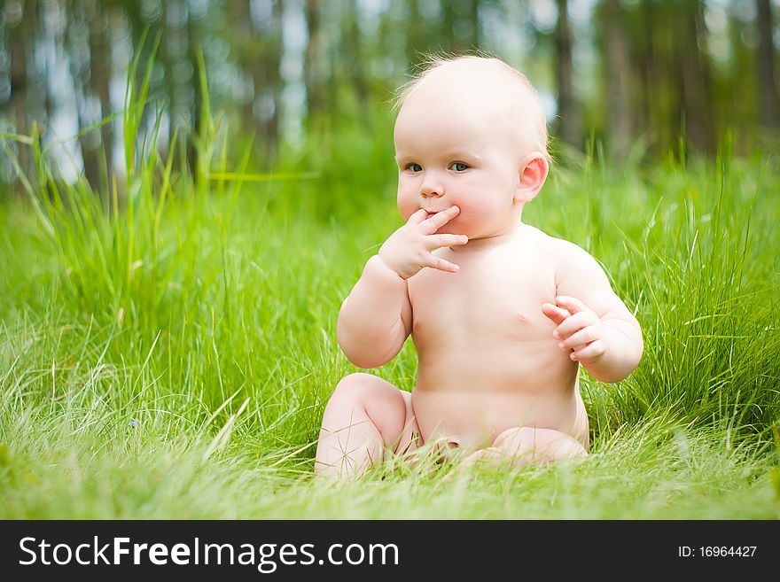 Baby sitting on green grass with fingers in mouth