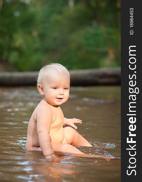 Little girl sitting in the river water on sunset.