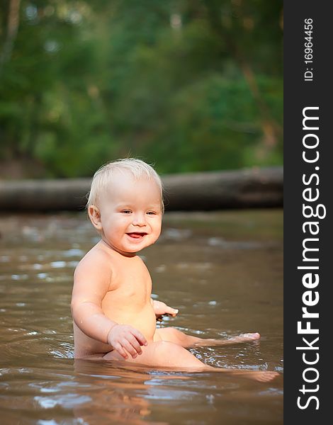 Little girl sitting in the river water on sunset.