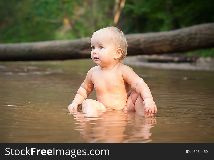 Little girl sitting in the river water on sunset