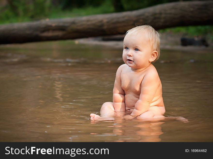 Little girl sitting in the river water on sunset.