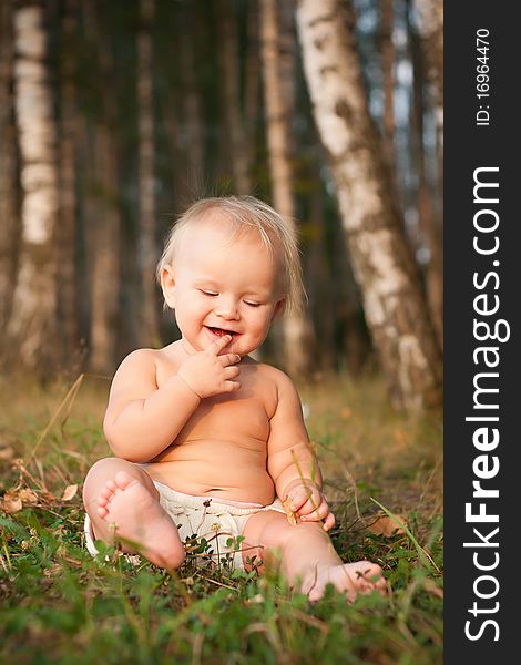 A little girl sitting on green grass in the park near forest