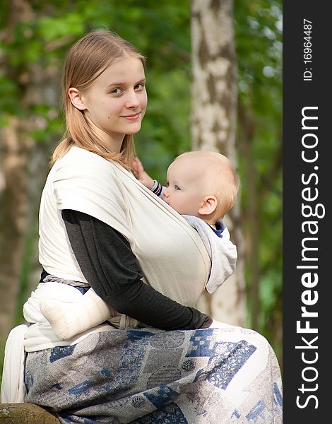 Mother sit  with daughter in sling in park. Mother sit  with daughter in sling in park.