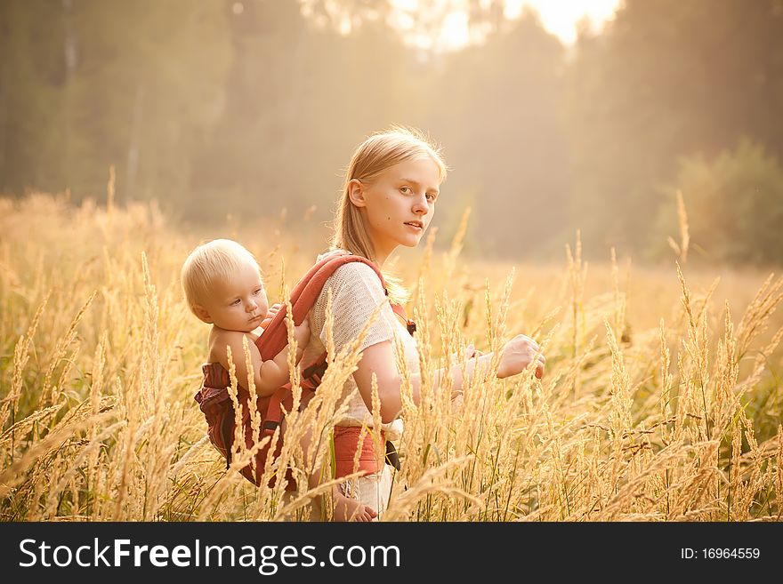 Mother and daughter walking near forest by the road in the wheat field on sunset.