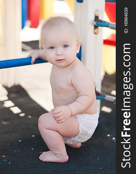 Littele baby play on playground holding stairs by hand and sit