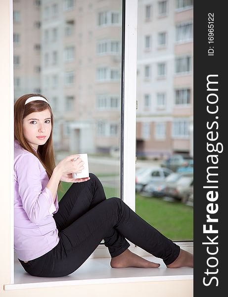 A girl with a cup is sitting on the window-sill. A girl with a cup is sitting on the window-sill