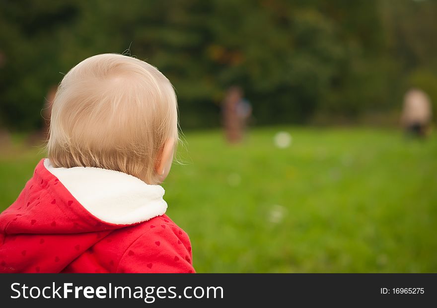 Young adorable baby stay on grass in park watching ball game. Young adorable baby stay on grass in park watching ball game