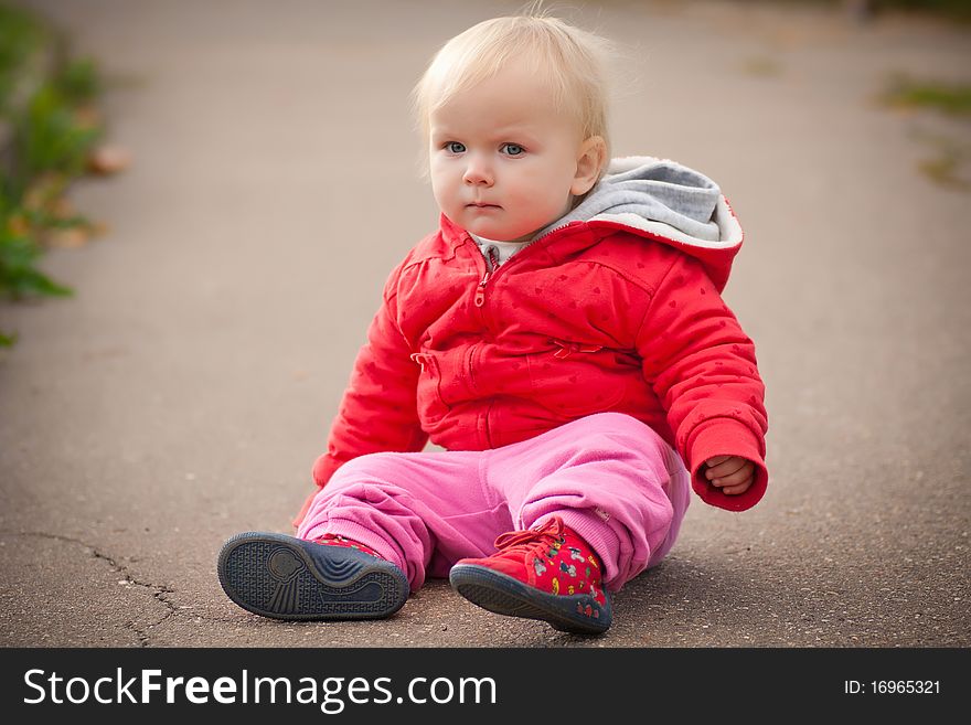 Young adorable baby sit on asphalt road and look to camera