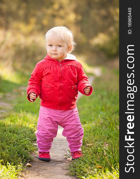 Young adorable baby walking by the road in field near forest