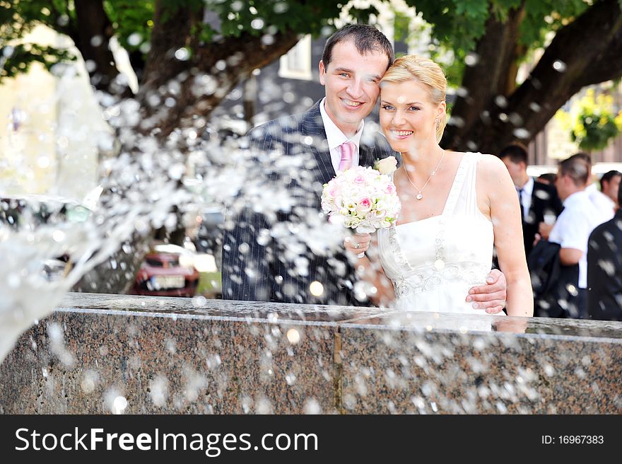 Bride and groom stand near fountain