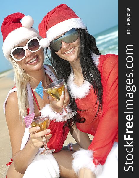 Two young sexy women in christmas suit with two martini glasses on the beachfront. Two young sexy women in christmas suit with two martini glasses on the beachfront