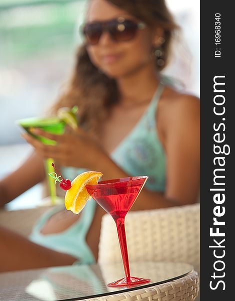 A glass of martini against young woman in sunglasses enjoying her summer vacation. A glass of martini against young woman in sunglasses enjoying her summer vacation