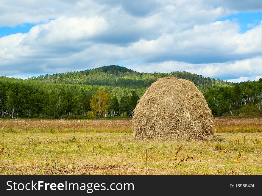 Blue sky and clouds over green hills with haystack. Transbaikalian landscape