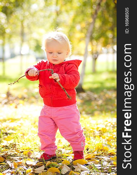 Young cheerful baby play with wooden brench under trees in park