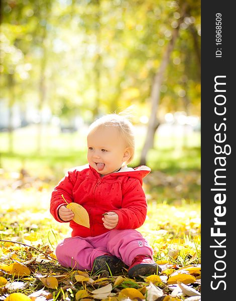 Young cheerful baby play with yellow leafs under trees in park